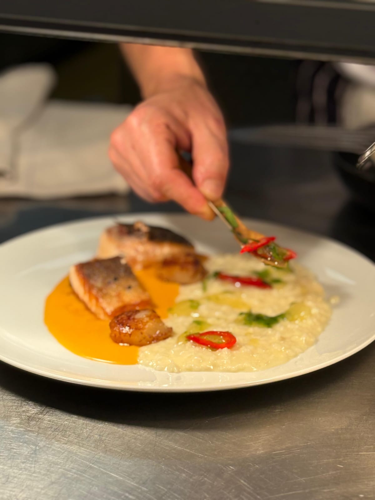 Adrian plating sea bass and scallops with risotto and red chilli in the kitchen
